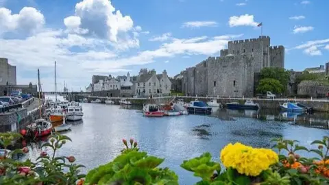 Castletown Harbour, with boats moored either side and blue skies above. Castl Rushen sits on the harbourside on the right.