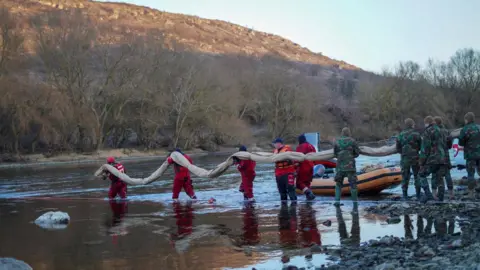Men in red carry a boom into the water to prevent oil spilling in the River Dniester
