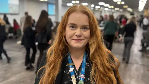 A woman with red hair wearing a black blazer in a conference room.