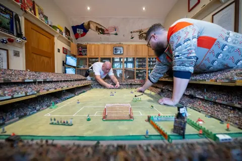 Justin Setterfield/Getty Images Penggemar Subbuteo bermain di meja buatan tangan di rumah Stephen Morton pada 29 Desember 2024 di Essex, Inggris. 