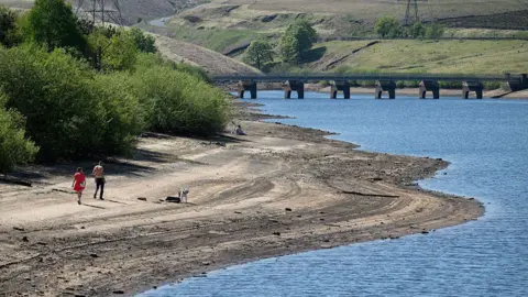 People walk their dog on the dry banks of a reservoir, which have been partially revealed by a falling water level.