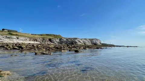 A view of Harrington coastline. Clear, shallow water stretches out before a rocky shore.