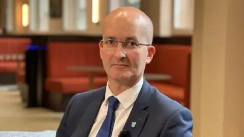Mid shot of a Prof Noel Purdy with glasses, and a blue suit.