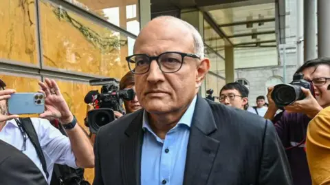 Getty Images Subramaniam Iswaran wearing glasses and a suit surrounded by people with cameras