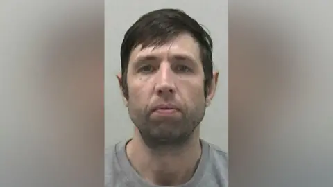 Mugshot of Ormston. He has faint black stubble and thick dark hair swept across his forehead