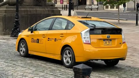 @EGGBOY_03 A bright yellow American cab on the cobbled stones of St George's plaza