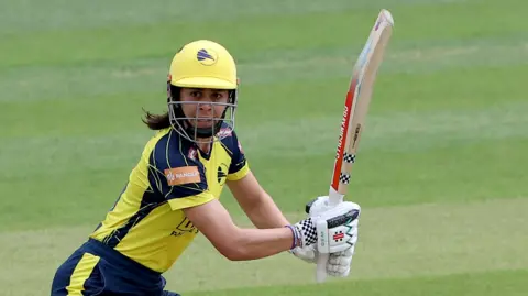 Maia Bouchier, in yellow and blue kit, plays a shot for Hampshire Hawks against Essex on 7 June