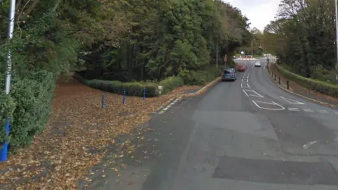 Google The turn off for Governor's Dip at the Victoria Road junction on the A2. The road is covered with leaves and there are blue traffic bollards in place. The road in front stretches out towards another roundabout at Governor's Road and there are trees lining either side of the carriageway.