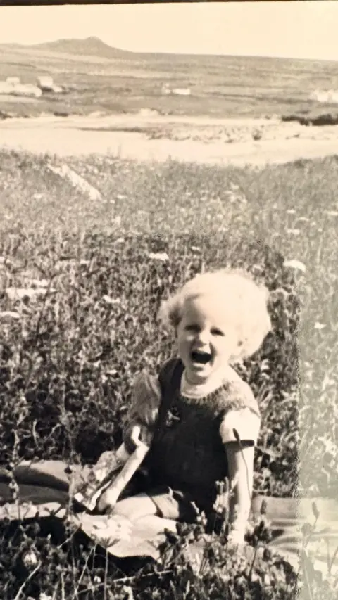 Maggie O'Farrell black and white photo of Maggie as a toddler blonde hair -- mouth open kneeling down on the ground rugged landscape of Ireland behind her