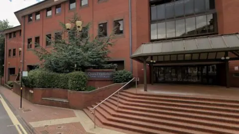 The entrance of a large red brick building, which has a number of steps up to the wide glass front doors. There is a large sign outside that says law courts.