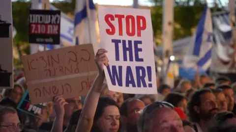 Protesters march holding aloft signs, one reads 'Stop the war!'