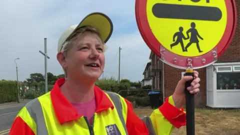 Stella is wearing hi-vis yellow and orange jacket and is holding a Lollipop STOP sign