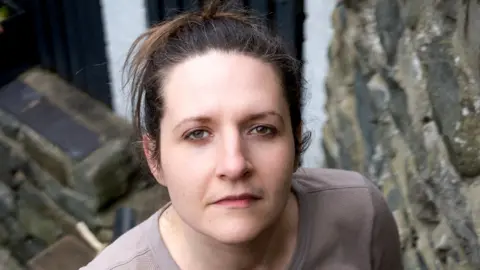 Ruth has dark hair and is looking directly at the camera.