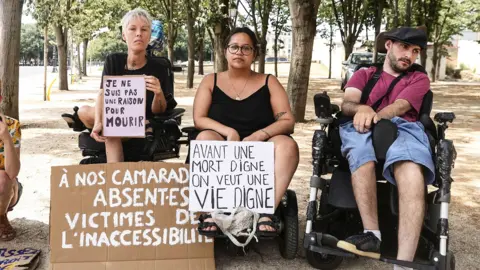 EPA Protesters in wheelchairs hold up signs reading "I am not a reason to die " and "Before a dignified death, I want to see a dignified life"