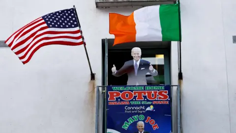 Reuters A cardboard cut-out of Joe Biden. Above the cut-out there is an Irish flag and an American flag. There is also a sign which reads 'WELCOME HOME POTUS'