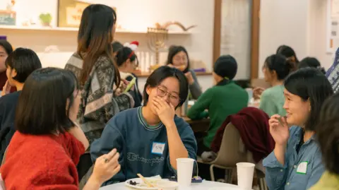 Courtesy Kyla Kim Women sit around a table laughing at the Ha Mina book talk.