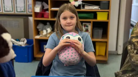 Eight year old girl in a classroom wearing school uniform holding stuffed toy 