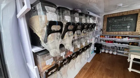 Tom Jackson/BBC Plastic containers of herbs and spices and items such as porridge oats and lentils with nozzles to collect them from inside the van.