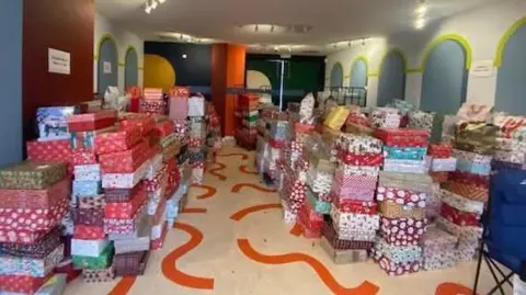 Sheffield Shoebox Appeal A room full of stacks of shoeboxes wrapped in Christmas wrapping paper.