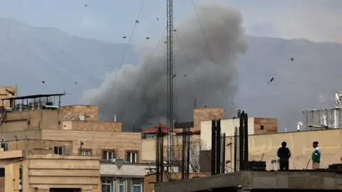People watch as smoke rises in central Tehran after an airstrike in Tehran, Iran, 02 March 2026.