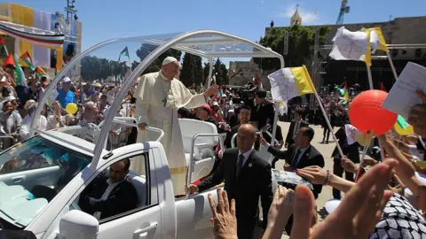 AFP via Getty Images Pope Francis waves to the crowd from his popemobile as he arrives at Manger Square before presiding over a Mass outside the Church of the Nativity, in Bethlehem, in the occupied West Bank (25 May 2014)