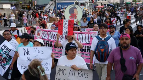 CONNIE FRANCE/AFP via Getty Images Demonstrators hold signs against violence during a national march against organized crime and hired assassinations, called by social and political organizations in Lima on March 21, 2025.