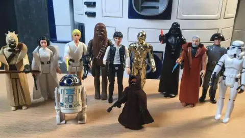 A number of vintage Star Wars figures lined up including Luke Skywalker, Han Solo and Chewbacca, droids C3PO and R2-D2, and Darth Vader
