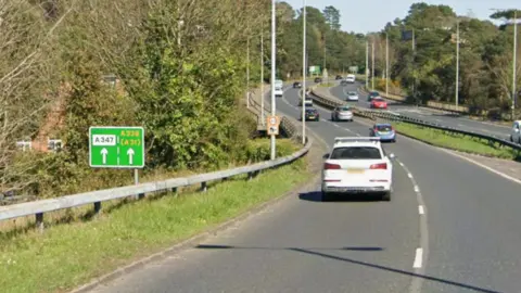 A view of the A338 Wessex Way between the Bournemouth West Roundabout and the Richmond Hill Roundabout. Some cars are driving on the road. It is sunny.