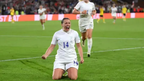 Getty Images Fran Kirby of England celebrates with team mates after scoring the team's fourth goal during the UEFA Women's Euro 2022 semi final match between England and Sweden at Bramall Lane. She kneels on the grass celebrating, while her team mates rush towards her.