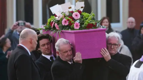 At the funeral of Linda Nolan at St Paul's Church, a pink coffin. There are pink and red flowers on it.