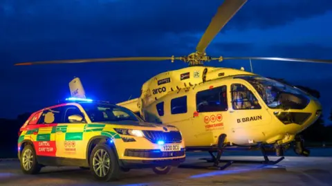 Yorkshire Air Ambulance One of the yellow Yorkshire Air Ambulances, next to an ambulance car, taken at night.