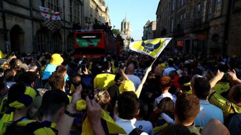 Thousands of fans and an open-top bus in St Aldate's in Oxford, with Tom Tower at Christ Church College in the background 