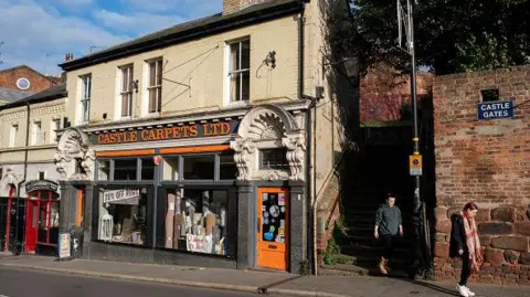 Getty Images Independent carpet shop Castle Carpets is at Castle Gates in Shrewsbury. There are steps next to it and older brick walls.