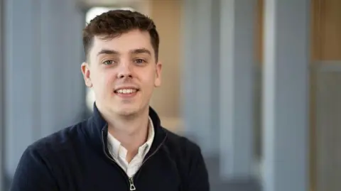 Ulster University Todd Gowdy, a man with short dark hair, wearing a blue zipped top and a white shirt.