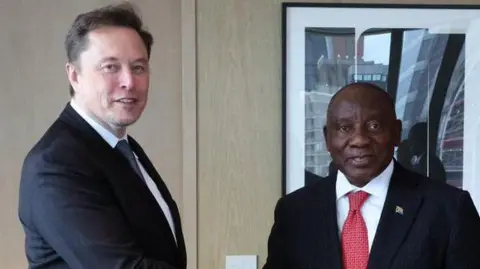 Elon Musk and Cyril Ramaphosa stand next to each other looking at the camera.