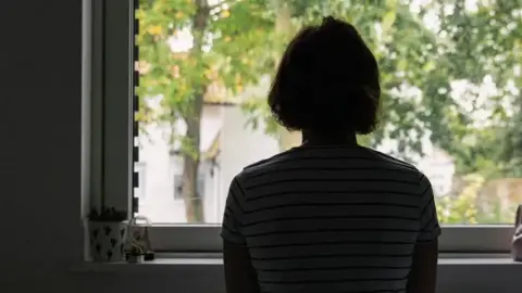 Woman in shadow looking out of window