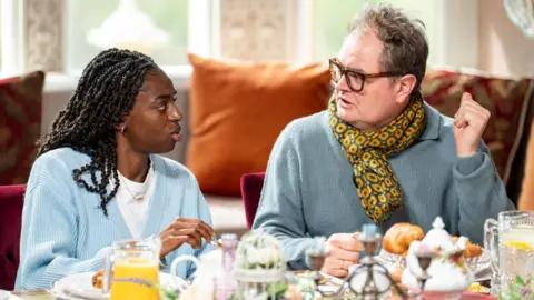 BBC Cat Burns and Alan Carr in the breakfast room on the Celebrity Traitors