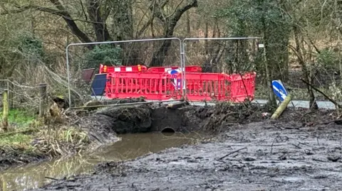 Edd Smith/BBC The road by the culvert that has been fenced off with metal and plastic fencing.