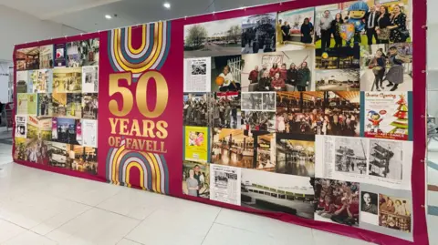 A large manufactured board with a maroon background with lots of different photos of the shopping centre from down the years on it. 