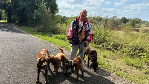Local Democracy Reporting Service A man walking 4 brown dogs smiles to the camera.