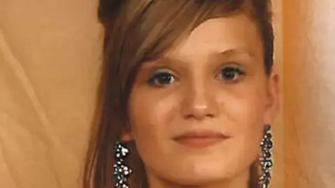 A close-up photo of Melissa's face. She has long brown hair with a sweeping fringe. She is wearing long silver and black earrings.