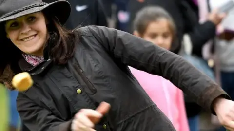 A woman in a wax jacket and hat throwing a Dorset Knob.
