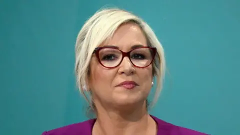 Getty Images Ms O'Neill has blonde hair tied back with a side fringe. She is wearing makeup, red glasses and a purple top.
