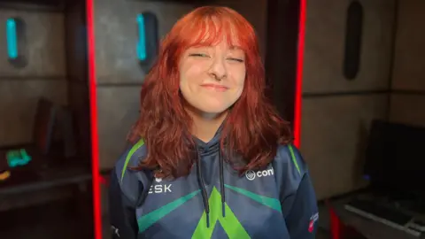 Arkay smiling at the camera wearing a blue and green Confetti Arrows hoodie