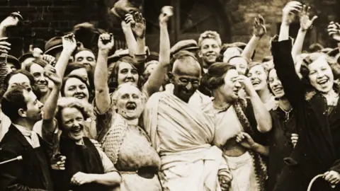 Getty Images Mahatma Gandhi with smiling workers at the Greenfield Mill at Darwen.