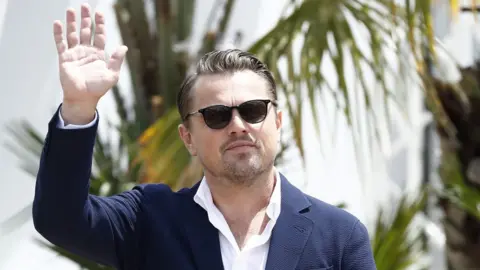 Getty Images Leonardo DiCaprio waving, behind him is a tree