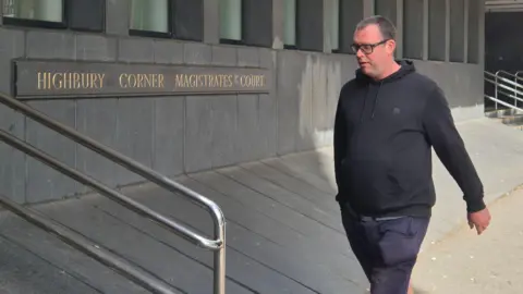 PA Media A man in a black hoodie walks towards a court. 