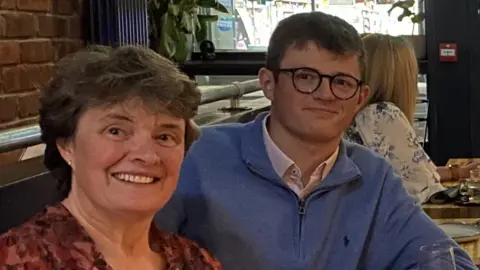 Susie Gear The image shows two people sat in a restaurant. A woman is sat on the right with a red top and a man in a blue jumper is sat on the left with glasses. 