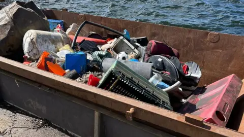 Cardiff Rivers Group A skip full of large discarded items that had been littered at Mermaid Quay in Cardiff Bay. They include a football and childrens car seat.
