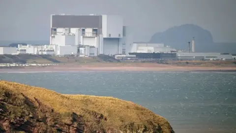 Torness nuclear power station stands in the middle distance beyond a grassy headland and the sea. 